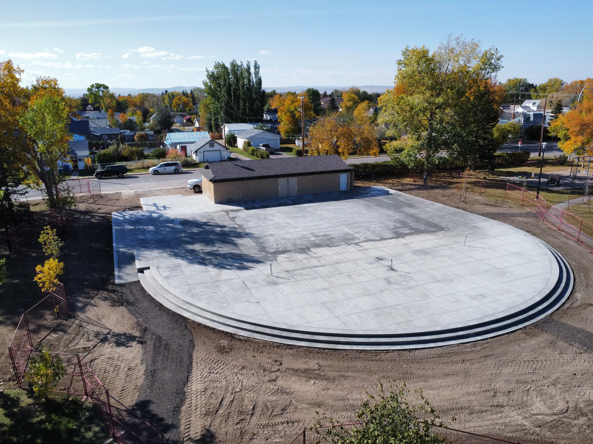 Aerial view of the finished curved concrete plaza with tiered seating steps beside a park building at Amundsen Park Plaza, built by Premiere Builders