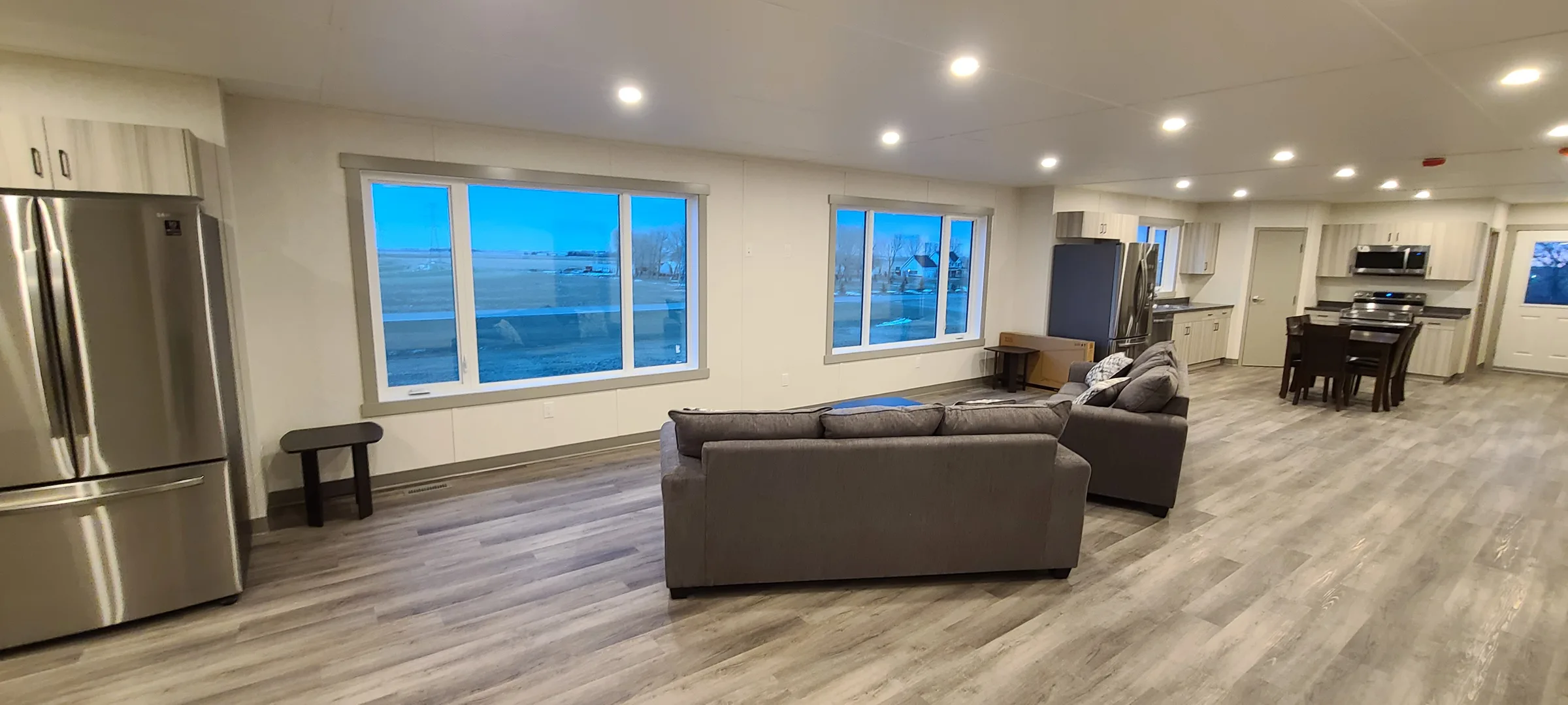 Living area with sectional sofa and large windows opening to the kitchen and dining space at Employee Housing Complex, built by Premiere Builders