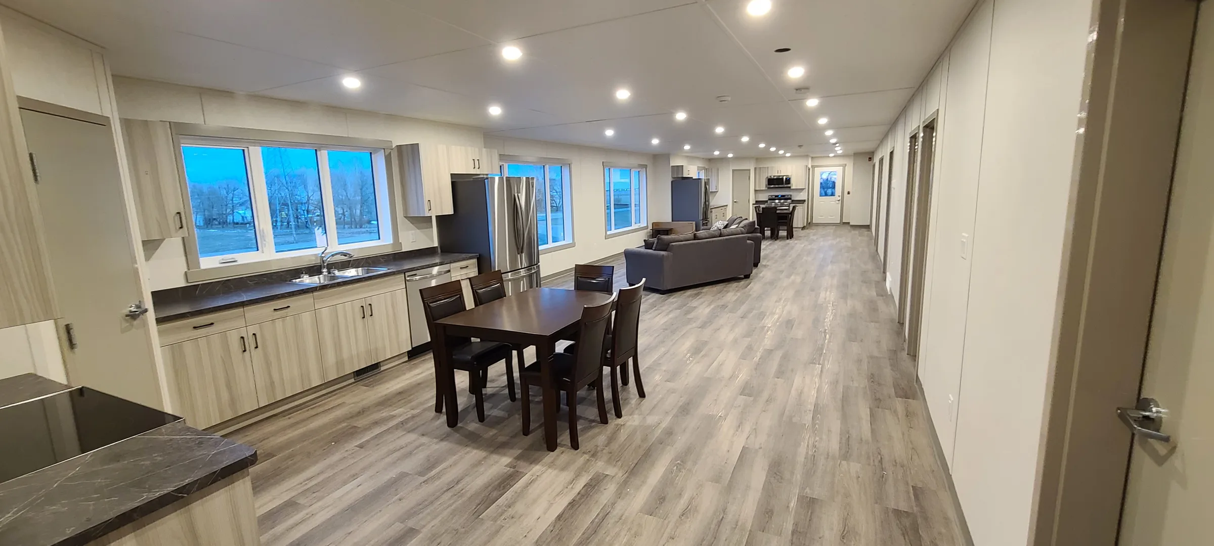 Long view through a shared suite with kitchen counters, dining table and pot lights at Employee Housing Complex, built by Premiere Builders