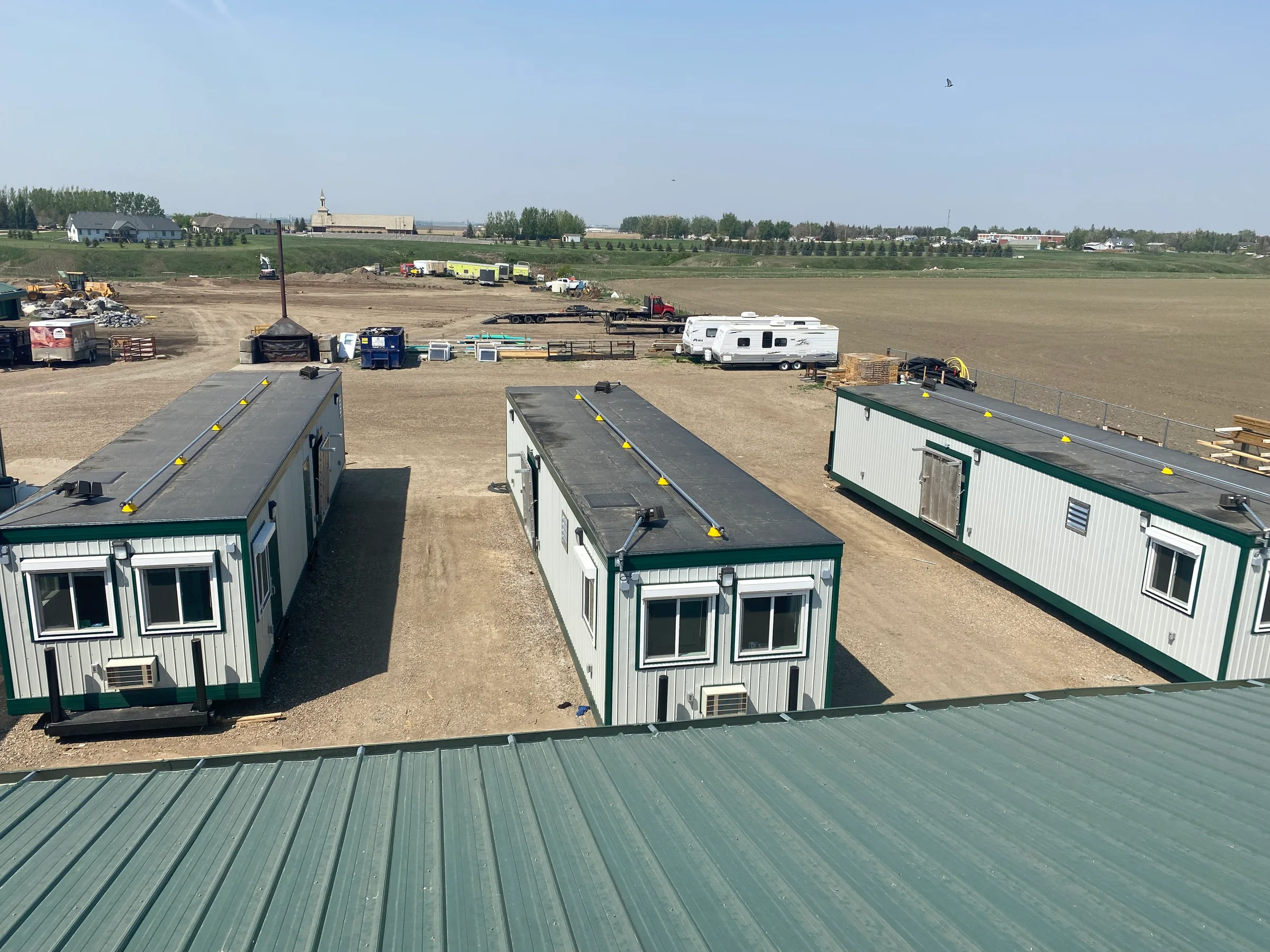 Elevated view of three completed modular units with green trim lined up in the yard before shipping at Incident Supply Units, built by Premiere Builders