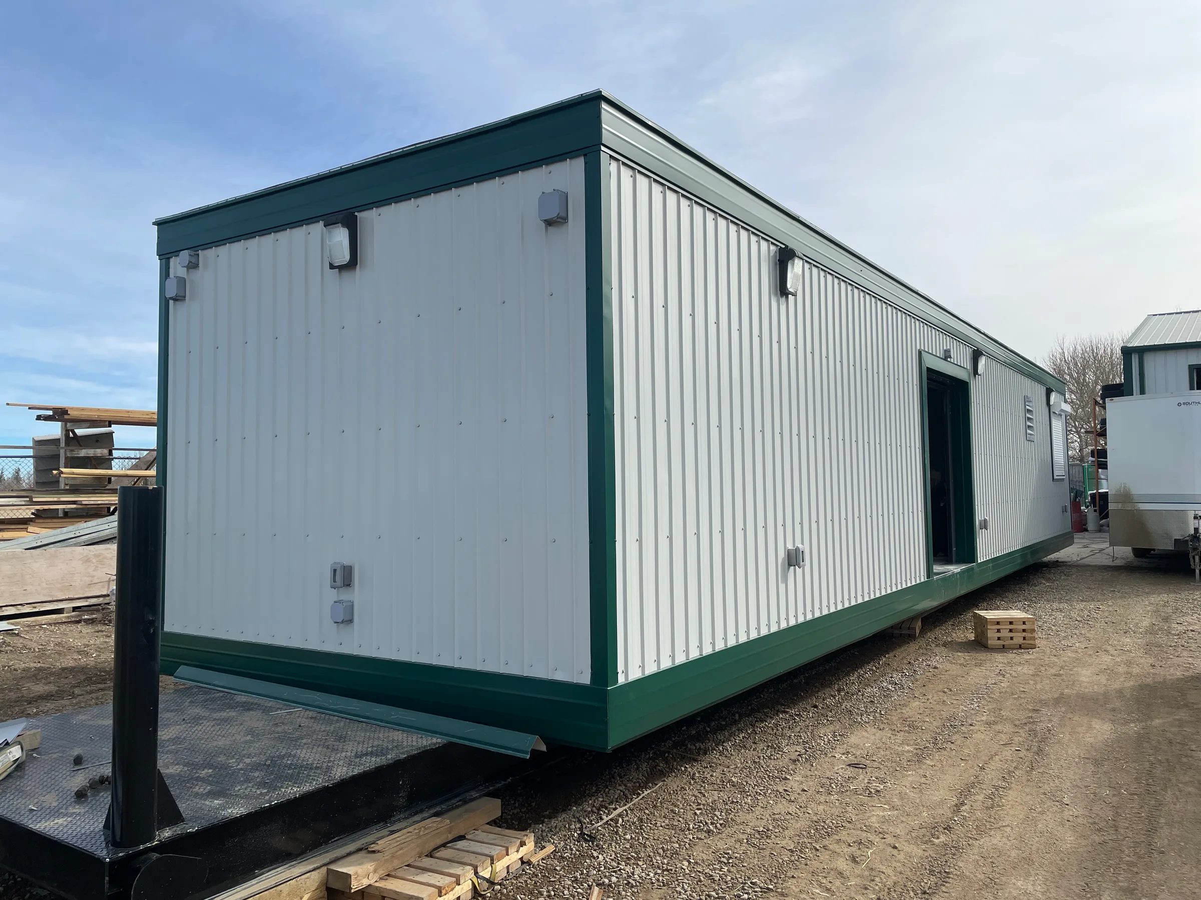 Finished modular incident unit with white ribbed metal cladding, green trim and exterior lights at Incident Supply Units, built by Premiere Builders