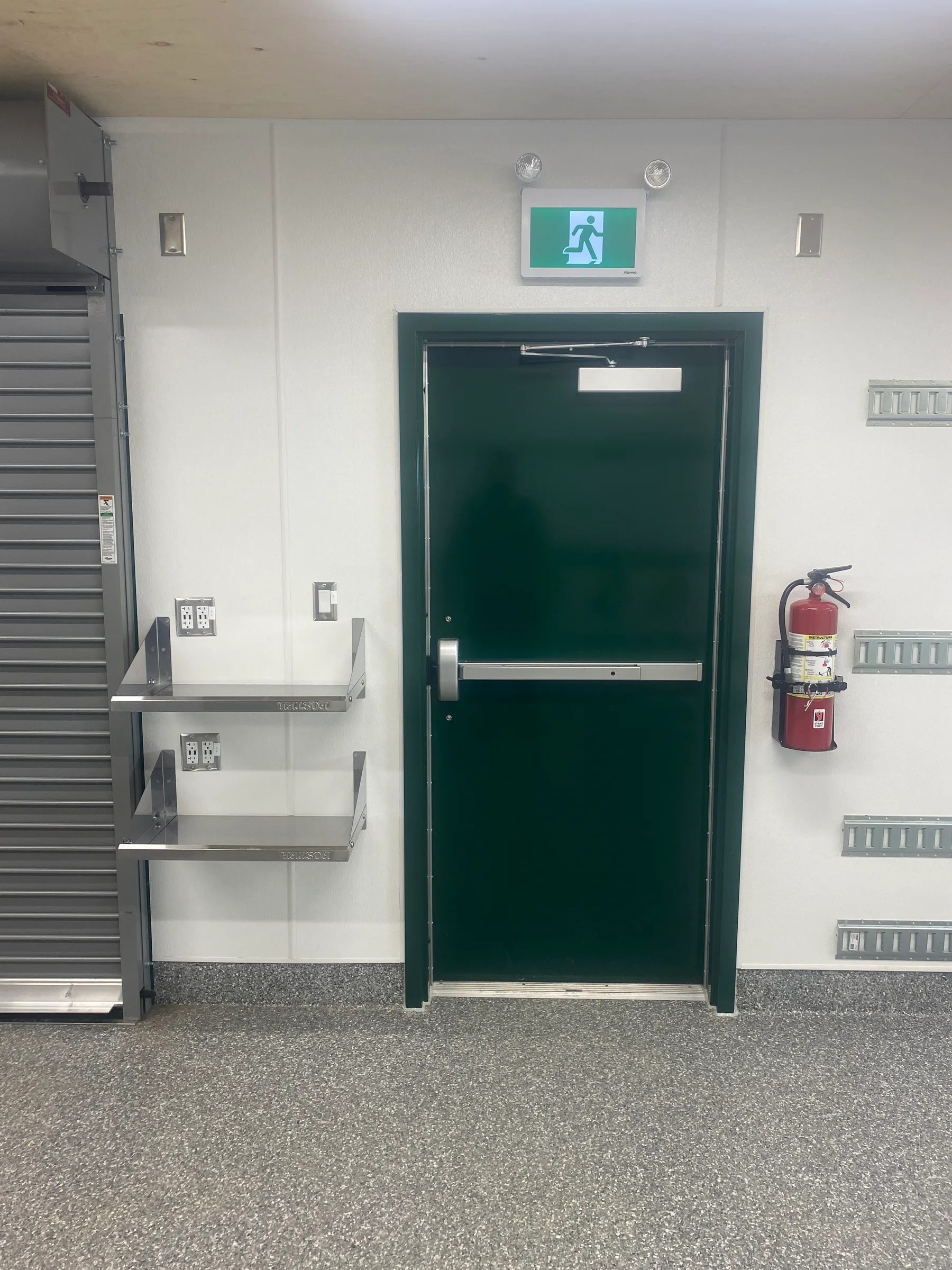 Interior of a modular unit with green steel exit door, stainless shelving and epoxy flooring at Incident Supply Units, built by Premiere Builders