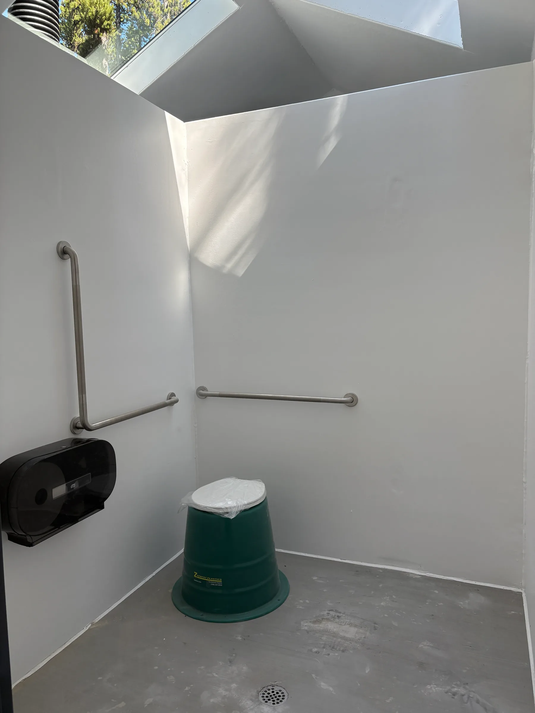 Clean vault toilet interior with white walls, grab bars, skylight and sealed floor at Kananaskis Region Vault Toilets, built by Premiere Builders