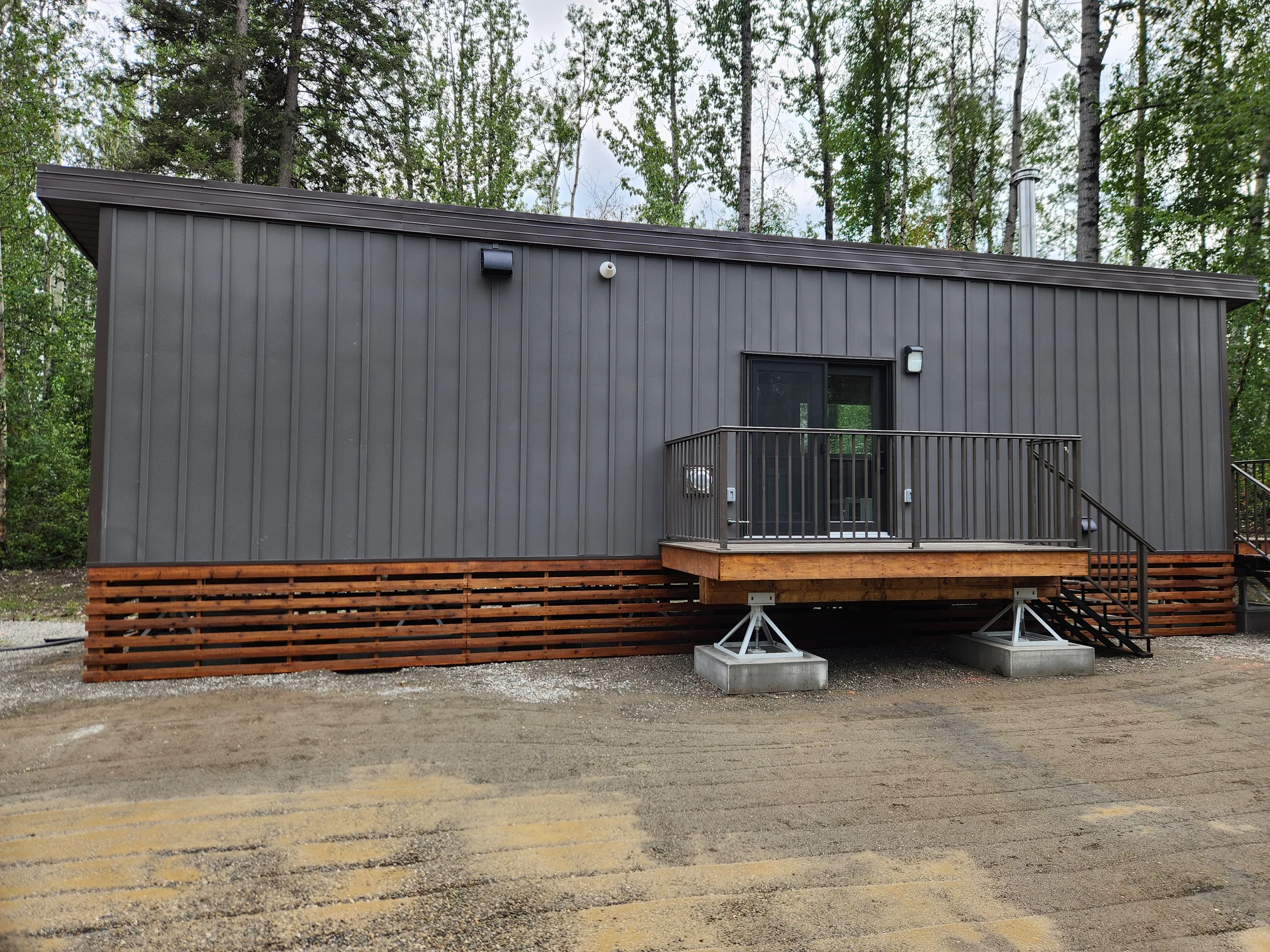 Completed modular cabin with railed entry deck on steel pedestal supports in a forest clearing at Liard River Park Ranger Cabins, built by Premiere Builders