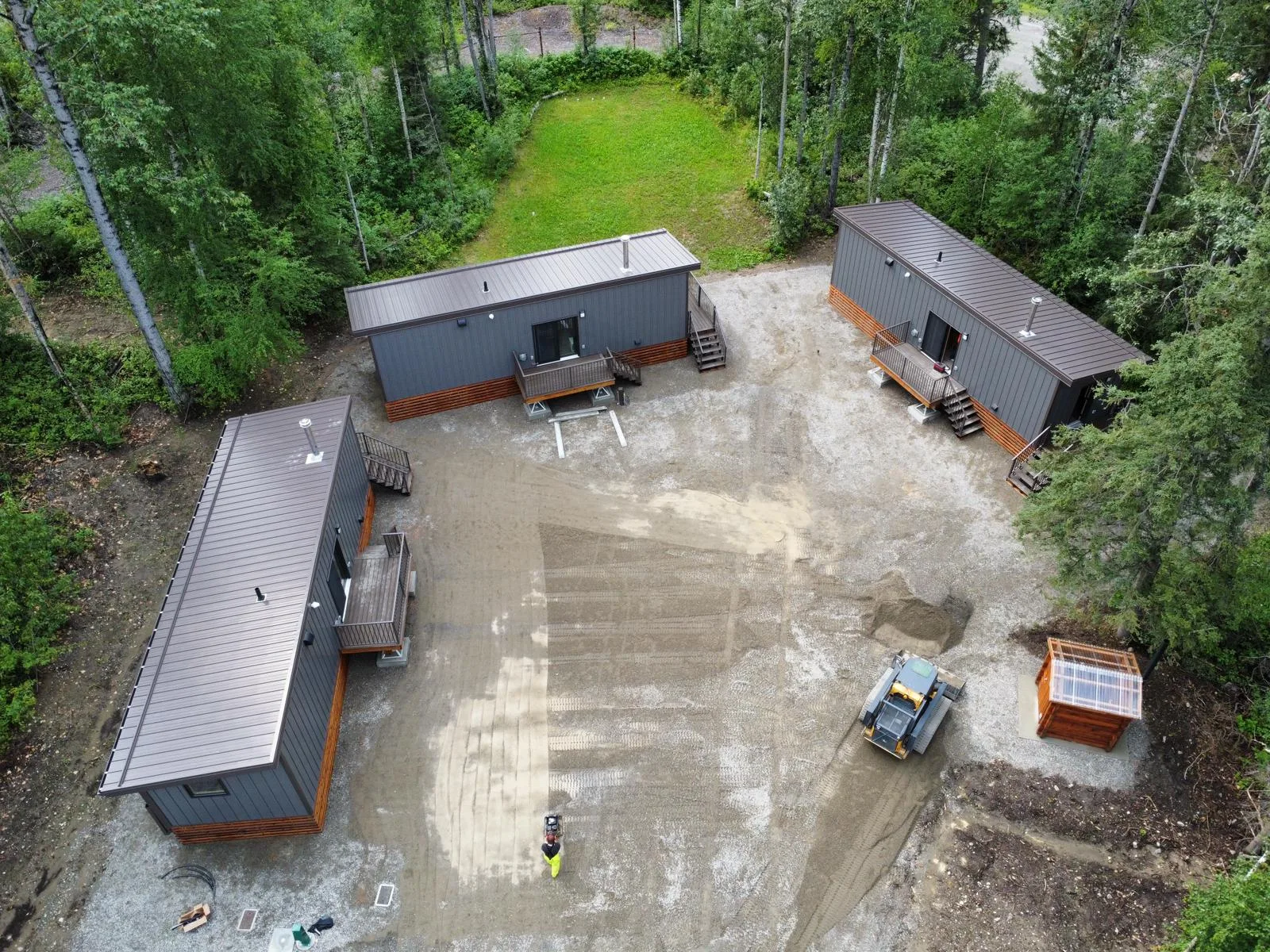 Aerial view of three completed modular cabins arranged around a gravel yard in the forest at Liard River Park Ranger Cabins, built by Premiere Builders