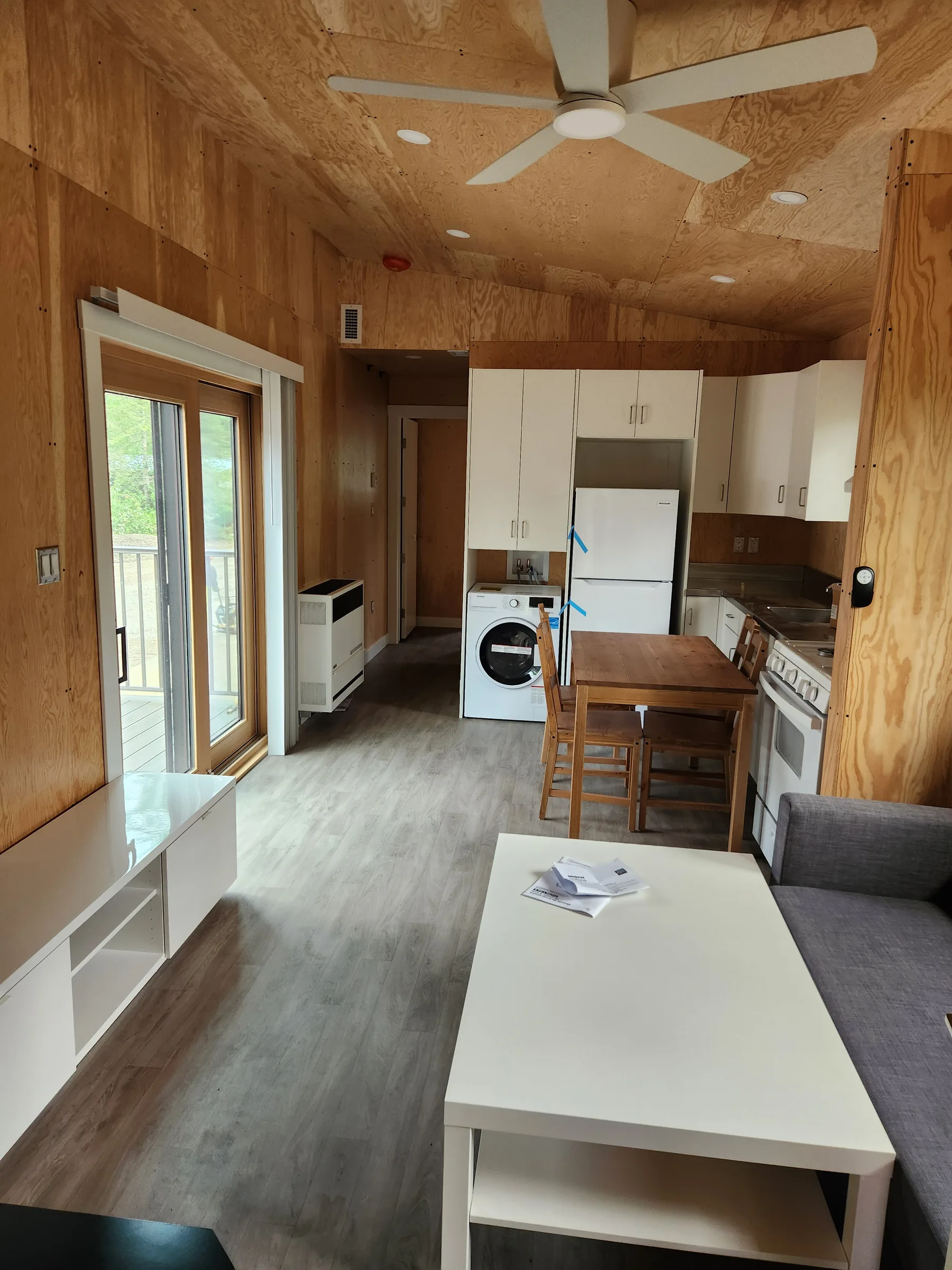 Open-plan cabin interior with living area, sliding patio door and kitchen under a vaulted wood ceiling at Liard River Park Ranger Cabins, built by Premiere Builders