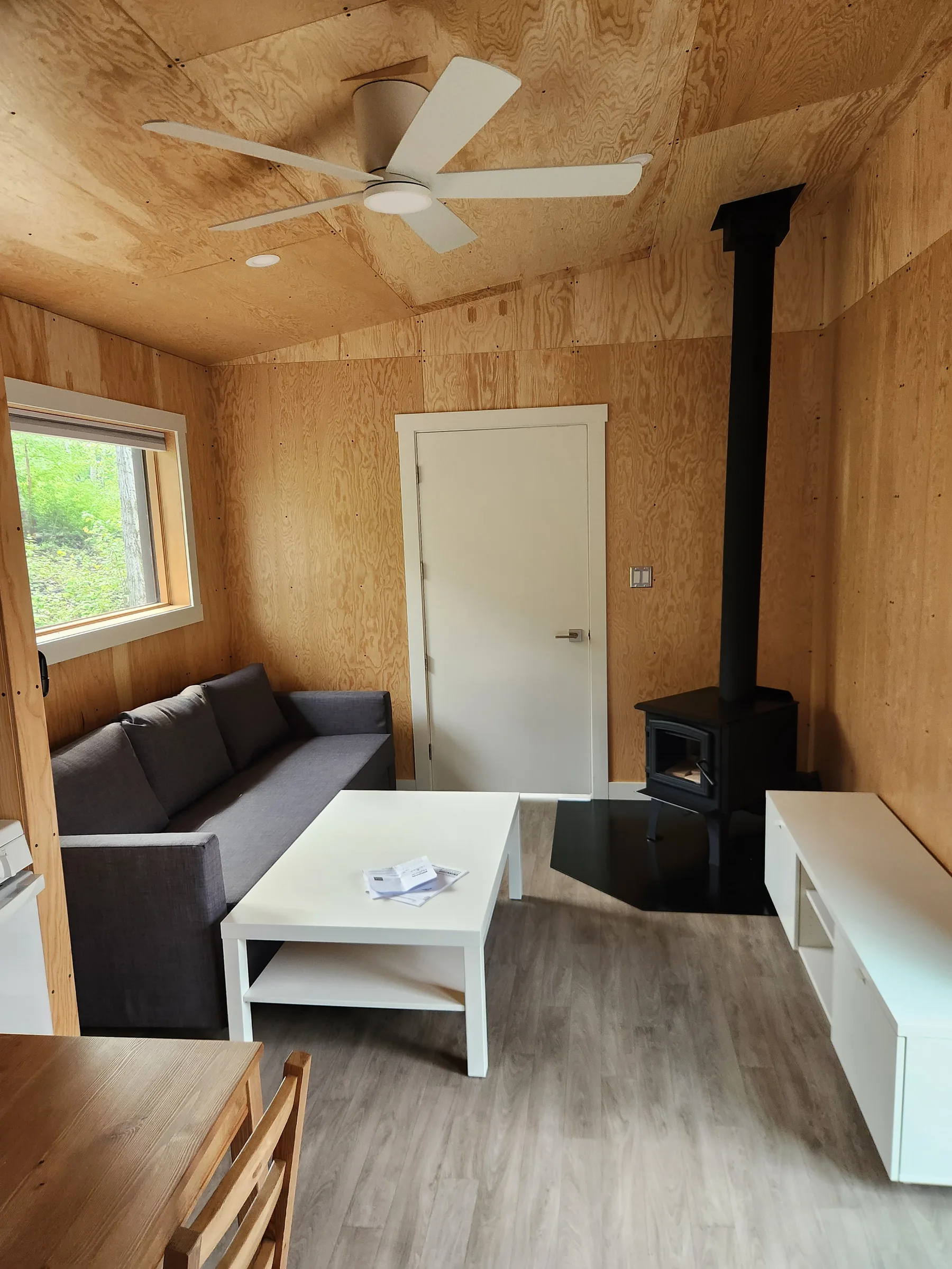Cabin living room with sofa, wood stove and ceiling fan beneath a vaulted plywood ceiling at Liard River Park Ranger Cabins, built by Premiere Builders