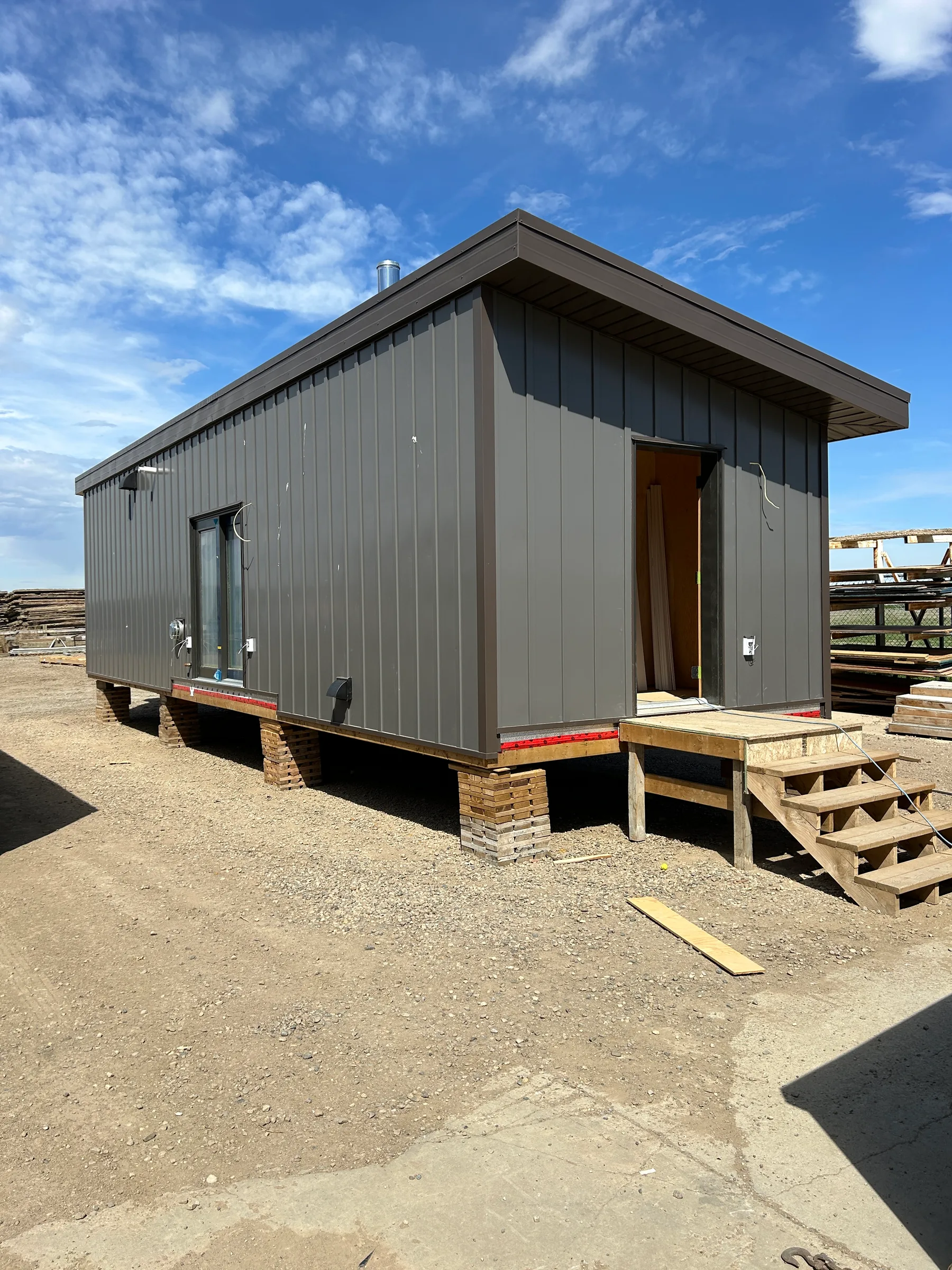 Modular cabin with dark metal siding nearing completion in the builder's yard under a blue sky at Liard River Park Ranger Cabins, built by Premiere Builders