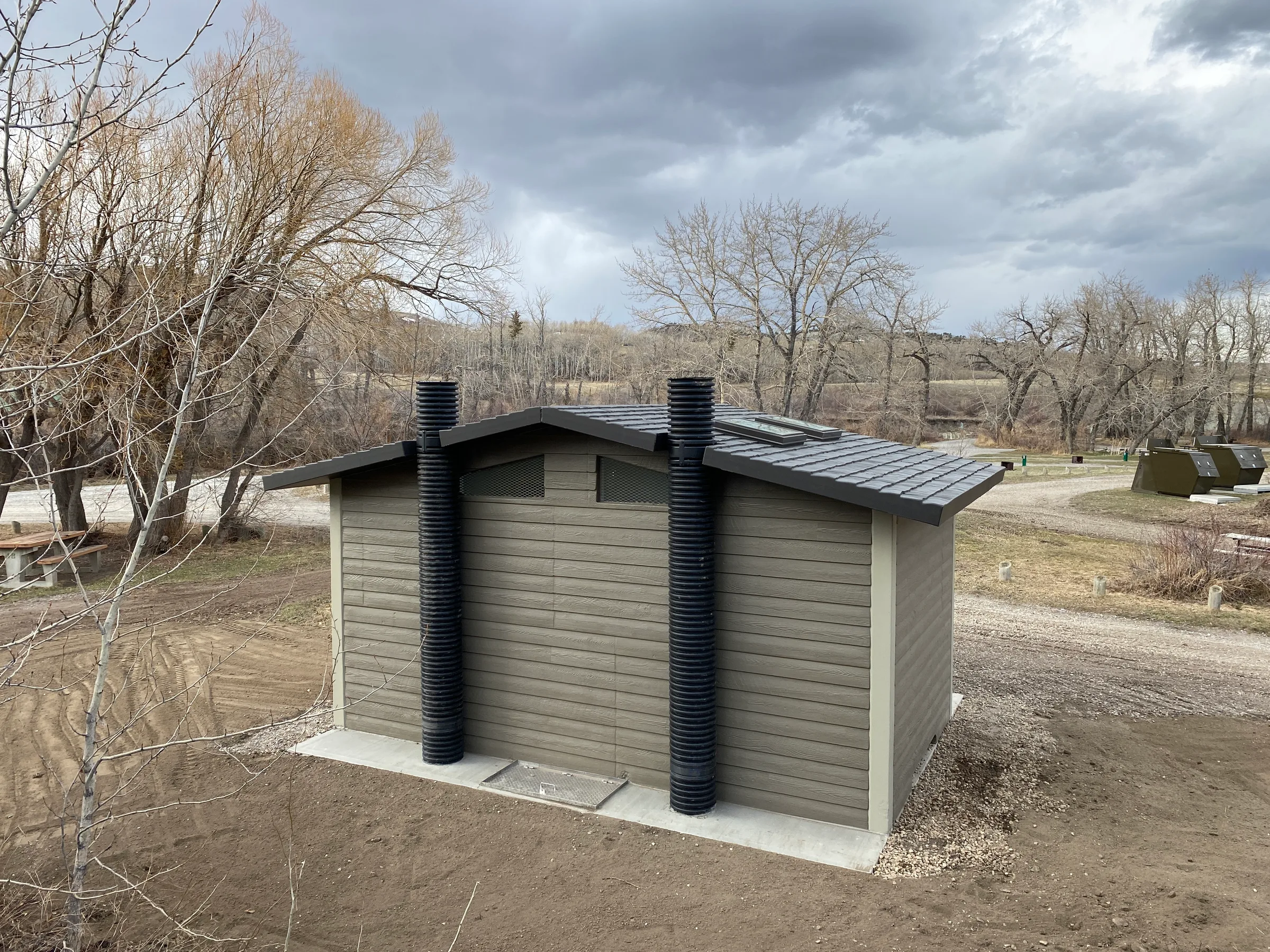 Rear of a new vault toilet showing twin black vent stacks and metal roof in a river valley park at Lundbreck Falls and Lake McGregor Vault Toilets, built by Premiere Builders