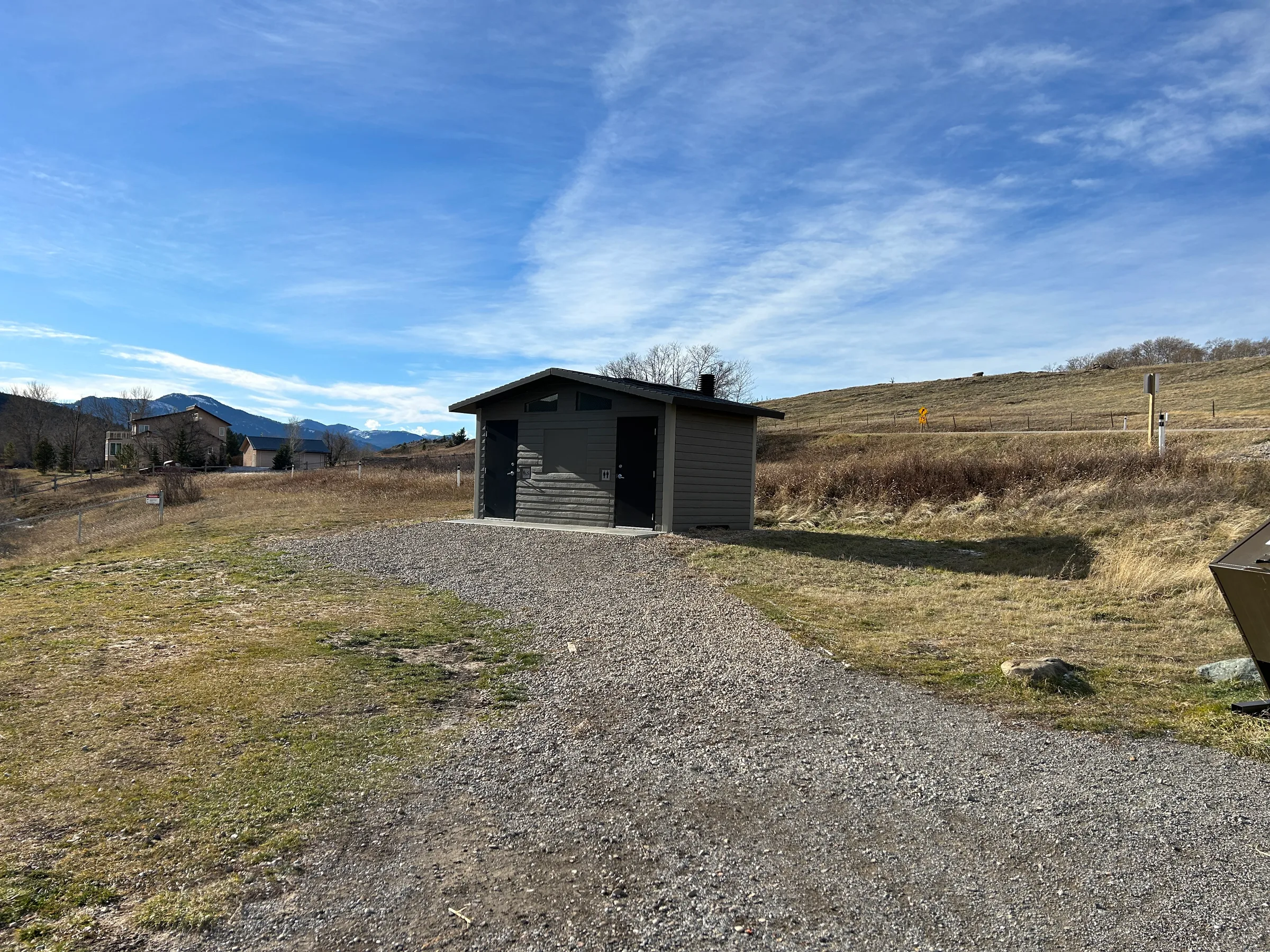 New vault toilet on a gravel path in open grassland with mountains on the horizon at Lundbreck Falls and Lake McGregor Vault Toilets, built by Premiere Builders