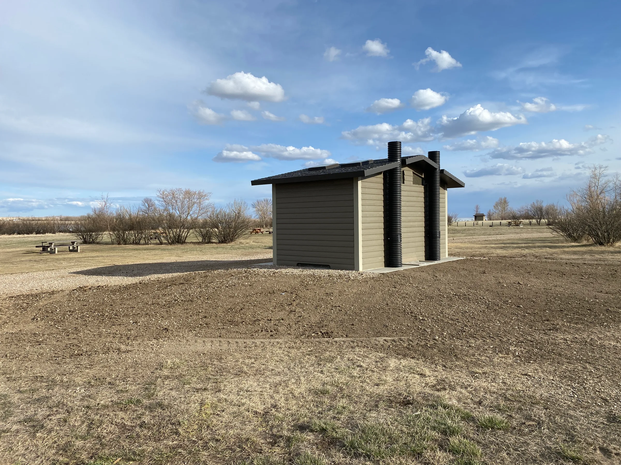 Completed vault toilet building with vent stacks standing in a prairie campground at Lundbreck Falls and Lake McGregor Vault Toilets, built by Premiere Builders