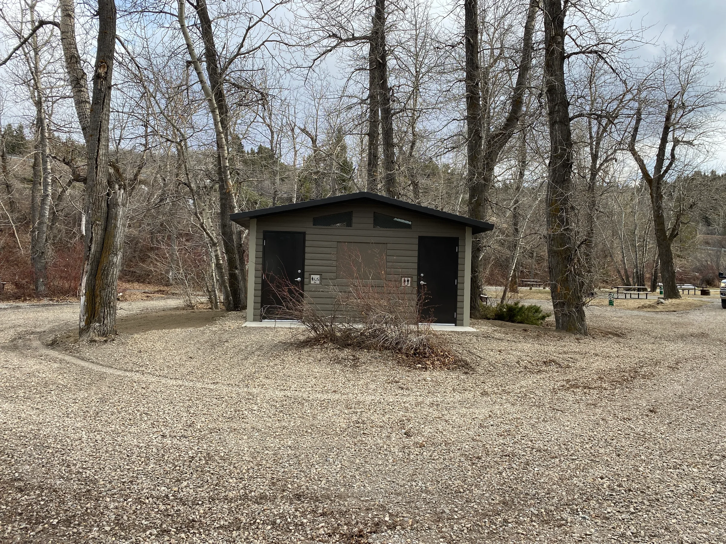 New vault toilet building set among cottonwood trees in a campground at Lundbreck Falls and Lake McGregor Vault Toilets, built by Premiere Builders