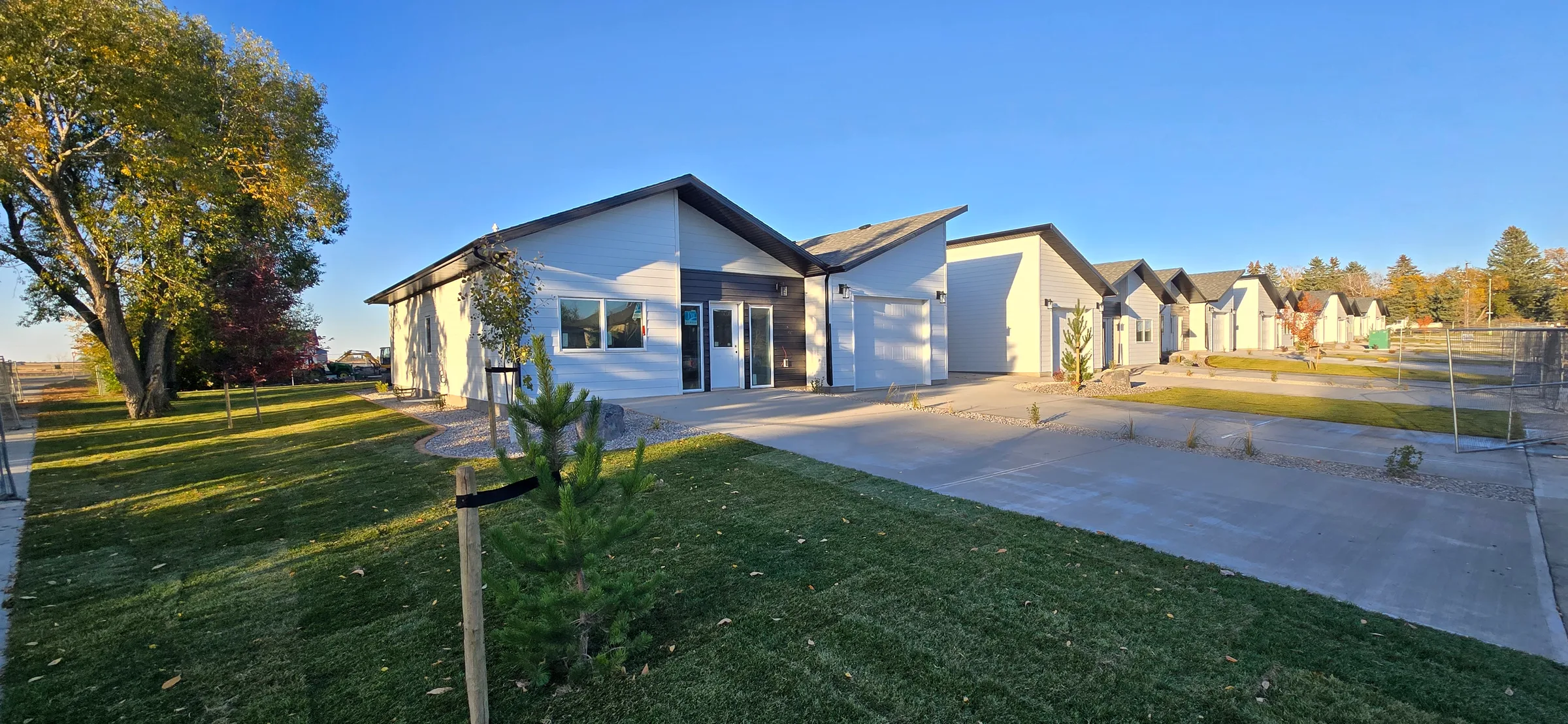 End of a completed fourplex with an attached garage and concrete driveway, cottages lined up behind at Porcupine Hills Lodge, built by Premiere Builders