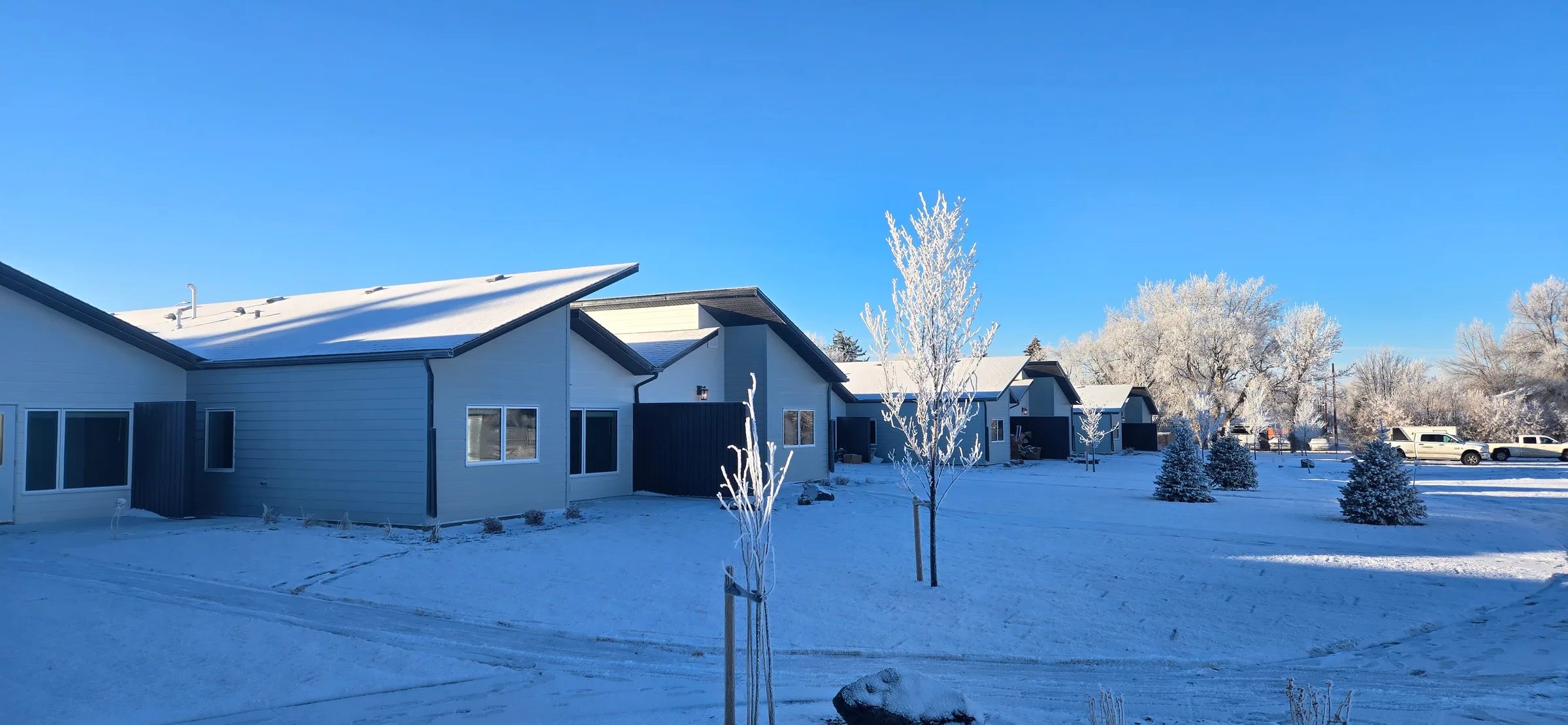 Seniors cottages with angled roofs under fresh snow and frosted trees on a clear winter morning at Porcupine Hills Lodge, built by Premiere Builders