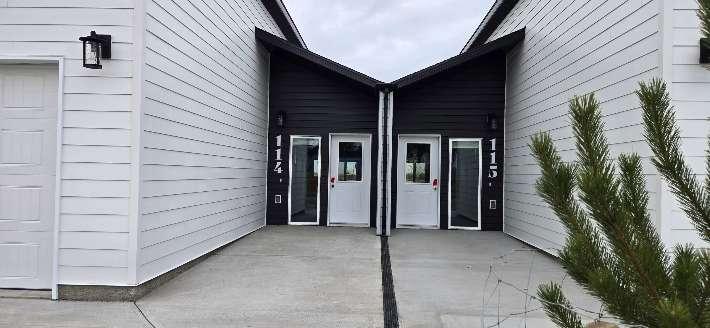Recessed entries of two units with dark siding, glazed doors and wall lanterns between garages at Porcupine Hills Lodge, built by Premiere Builders