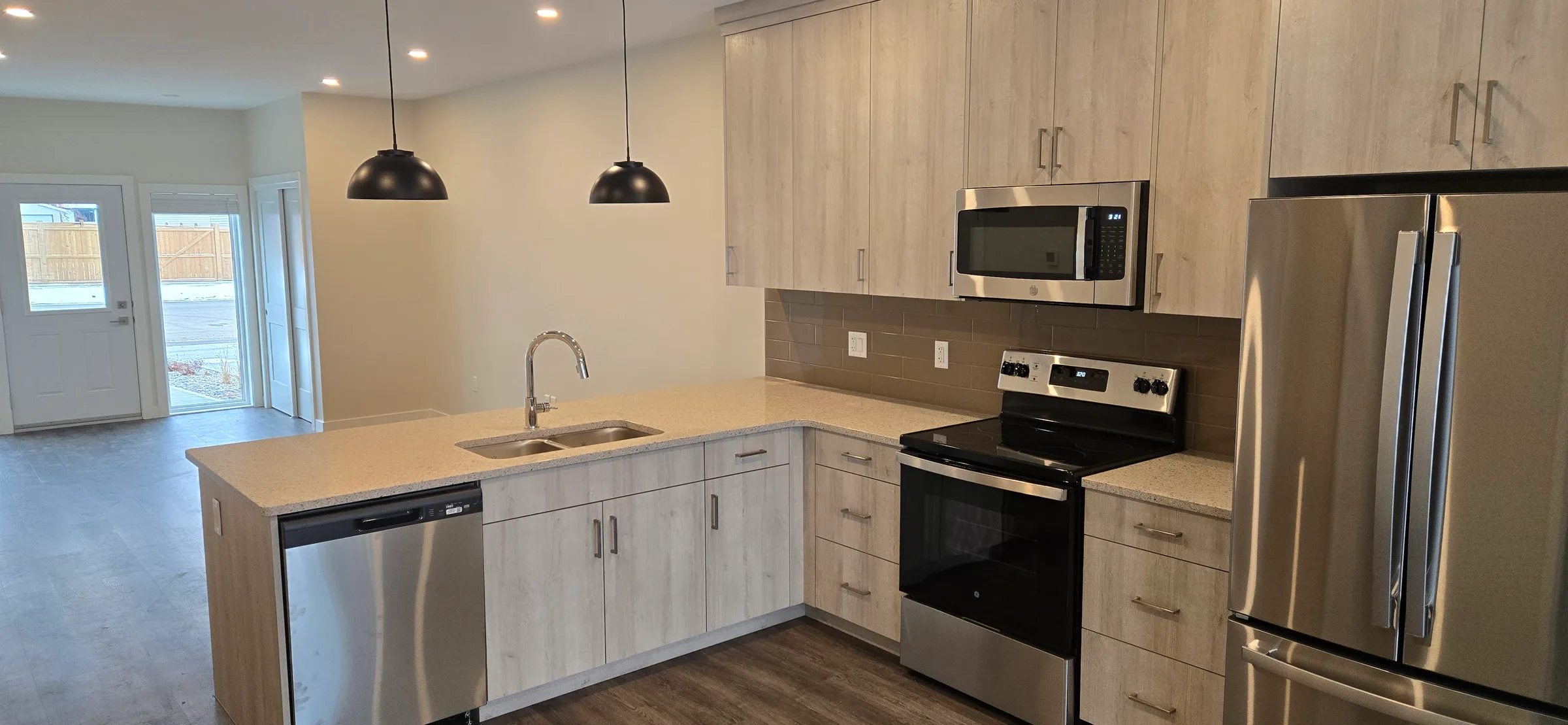 Unit kitchen with light wood-grain cabinets, quartz counters, stainless appliances and pendant lights at Porcupine Hills Lodge, built by Premiere Builders