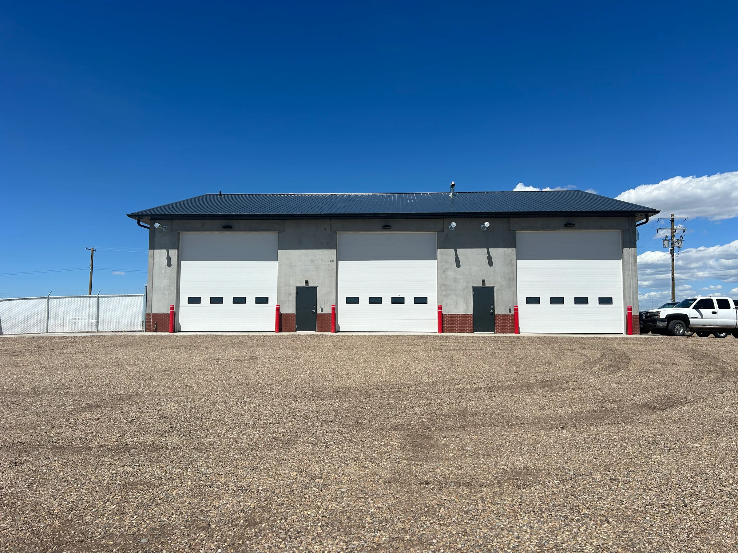 Completed fire hall with three white overhead apparatus bay doors under a blue sky at Seven Persons Fire Hall, built by Premiere Builders